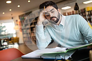 Exhausted young man student studying in a library