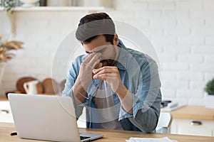 Exhausted young man take off glasses suffer from headache