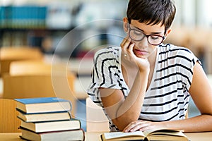 Exhausted young female studying and preparing for exam in college library. Education people concept