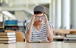 Exhausted young female studying and preparing for exam in college library. Education people concept