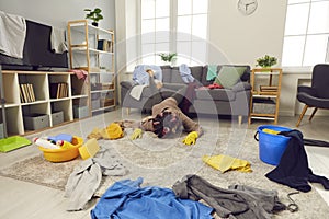 Exhausted young woman fallen on the floor while cleaning up her messy living-room