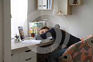 Exhausted young woman freelancer napping by desk after difficult workday photo