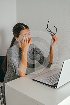 Exhausted young woman holding glasses and touching her eyes, overworking and eye fatigue from computer concept