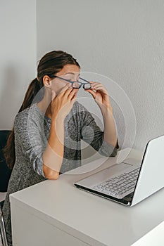 Exhausted young woman holding glasses and touching her eyes, overworking and eye fatigue from computer concept