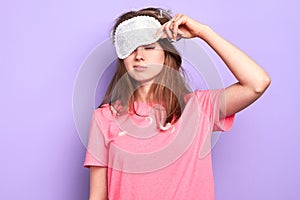 Exhausted young woman raises slightly her eye mask, trying to open sleepy eyes