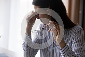 Exhausted young woman taking off eyeglasses, having blurry eyesight.