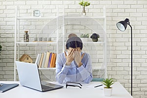 Exhausted young woman working overtime at office. Female employee suffering from work stress at her desk