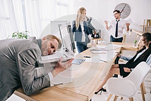 exhausted zombie like businessman sleeping on copier while his colleagues having conversation