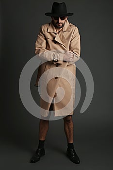 Exhibitionist in coat and hat on black background
