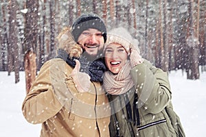 Exhilarated husband with thumb up hugging wife during the snowfall in the forest