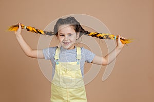 Exhilarated little girl pulling yellow kanekalon pigtails in different directions with hands, looking at camera smiling