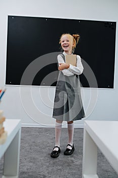 Exhilarated schoolgirl hugging textbook standing in front of a balckboard