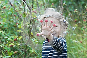 Exhilarated two years old blonde girl showing red garden raspberry fruits