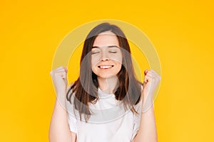 Exhilarated Woman Celebrating Big Win with Raised Fists - Excitement, Victory, and Financial Success Concept on Vibrant Yellow