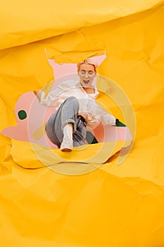 Exhilarated young woman tearing a hole through big sheet of cramped yellow paper photo