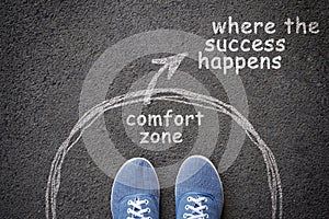 Exit from comfort zone concept. Feet in blue jeans sneakers standing inside circle and outward arrow chalky on asphalt.