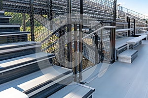 Exit, entrance, vomitorium at empty metal stadium bleacher seats along aisle with steps and railing.