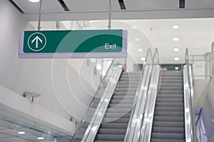 Exit information green board sign have blur escalator as background