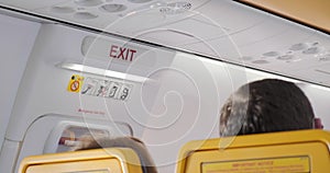 Exit sign next to seats with people inside an airplane cabin. Handheld, travel, emergency, interior