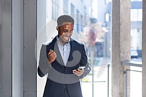 Exited African American Businessman Celebrating Achievement looking at Smartphone. Successful business man victory win with mobile