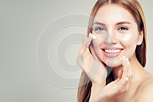 Exited beautiful woman with healthy clear skin applying moisturizing cream on her face, closeup portrait. Skin care