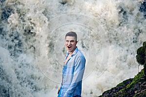 Exited happy man standing near water fall and looking at camera