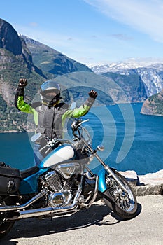 Exited woman motorcyclist glads to travel by motorcycle in Norway, Scandinavia. Viewpoint with Northern sea and fjords