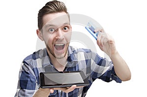 Exited young man, buying online via tablet, holding credit card in his hand