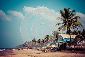 Exiting Anjuna beach panorama on low tide with white wet sand and green coconut palms, Goa, India