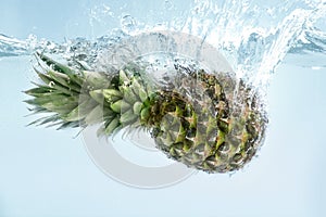 Exotic freshness. Juicy pineapple splashing into pure water on blue background