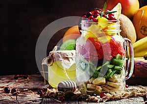 Exotic fruit salad with banana, kiwi, grapefruit, mango, cranberry and lemon juice and honey, served in a glass jar. Vintage wood