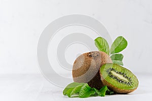 Exotic fruits closeup - juicy ripe fleshy kiwi with slice, drop juice and young green leaves in elegant white kitchen interior.