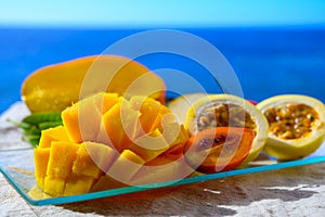 Exotic fruits, fresh ripe sweet yellow mango and passion fruits served on glass plate with blue seaview background