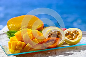 Exotic fruits, fresh ripe sweet yellow mango and passion fruits served on glass plate with blue seaview background