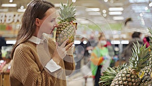 Exotic fruits for health. An attractive smiling woman in casual clothes chooses a pineapple in the supermarket