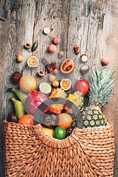 Exotic fruits in straw summer bag on wooden background. Top view. Copy space. Tropical fruits flat lay. Zero waste, plastic free