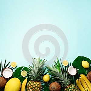 Exotic pineapples, ripe coconuts, banana, melon, lemon, tropical palm and monstera leaves on blue background with