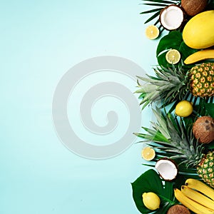 Exotic pineapples, ripe coconuts, banana, melon, lemon, tropical palm and monstera leaves on blue background with