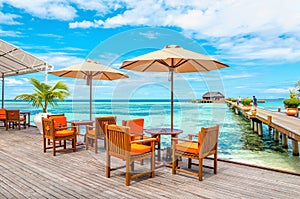 Exotic restaurant on the water, tables and chairs under sun umbrellas on the background of wooden bungalows