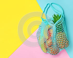 Exotic summer fruits in net bag on colorful background. Top view, copy space. Zero waste concept