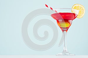 Exotic sunrise cocktail with red and yellow liquor, orange slice, straw on soft light mint color background and white wood board.