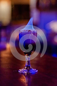 Exotic tropical alcohol cocktail burning with blue fire in the glass on the table during party