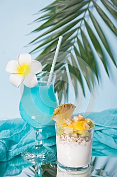 Exotic tropical fruit salad with muesli and yogurt in a glass with blue cocktail