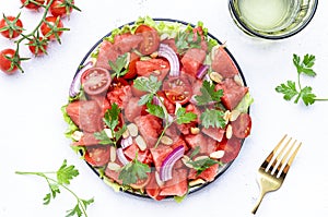 Exotic vegan salad with sweet watermelon, cherry tomatoes, red onion, peanuts and parsley, white table background, top view