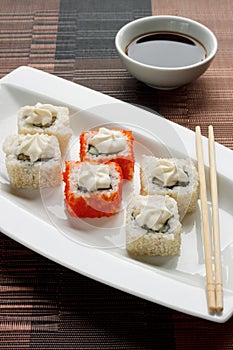 Exotically japanese seafood, roll and chopstick are lying on a white plate. Soy souce.