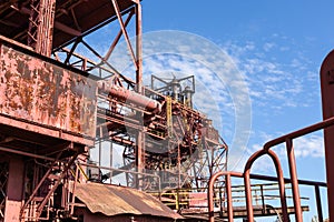 Expansive industrial steel manufacturing facility, rusted beams and girders, vivid blue sky