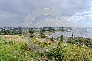 an expansive lake in the distance under a grey sky with some clouds