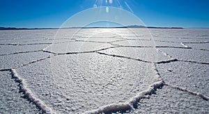 Expansive salt flats with hexagonal crust formations under a clear blue sky.