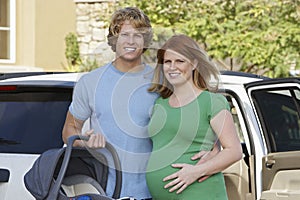 Expectant Couple With Cradle Standing By Car