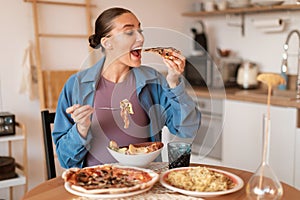 Expectant delights. Hungry pregnant woman eating pizza and salad, having desire for junk food, sitting in kitchen